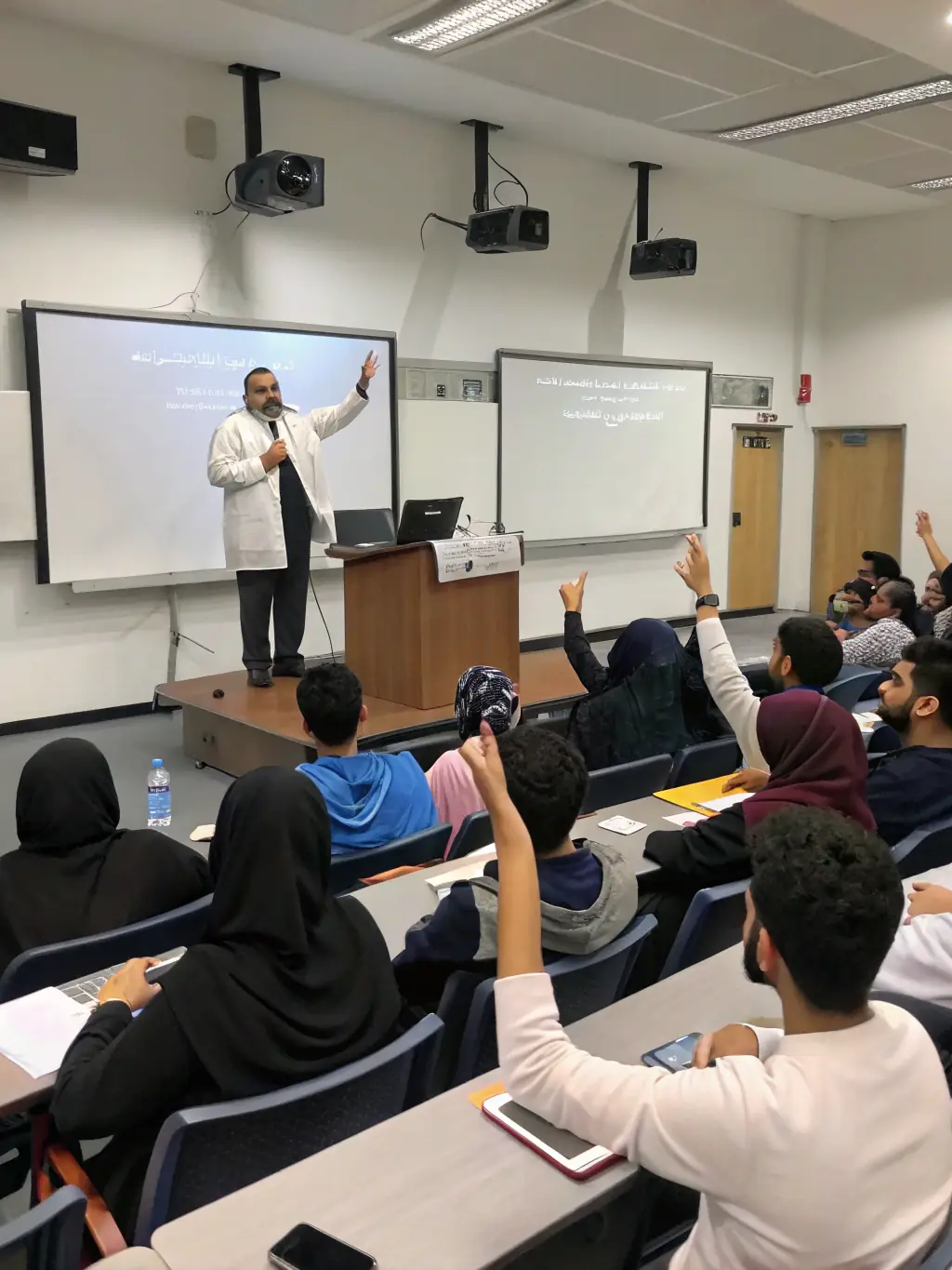 A Kuwait MCM faculty member delivering an engaging lecture to a class of undergraduate students in a well-equipped lecture hall.